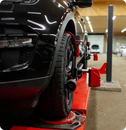 Carro preto em uma oficina mecânica recebendo os serviços automotivos de alinhamento de direção e balanceamento de rodas.