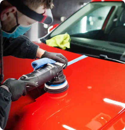 Capô de uma carro vermelho recebendo o serviço automotivo de cristalização de pintura por um homem branco com um equipamento preto.