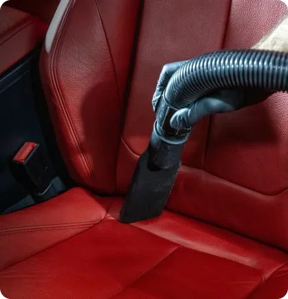 Estofado do banco de um carro, em couro vermelho, sendo aspirado no serviço automotivo de higienização automotiva.