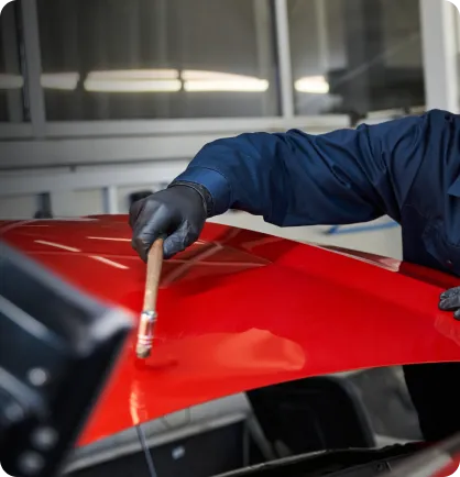 Prestador de serviço segurando um martelo realizando o serviço automotivo de martelinho de ouro em uma peça de um carro vermelho.