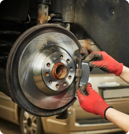 Prestador de serviço, utilizando luvas vermelhas, realizando o serviço automotivo de troca de pastilha de freio.