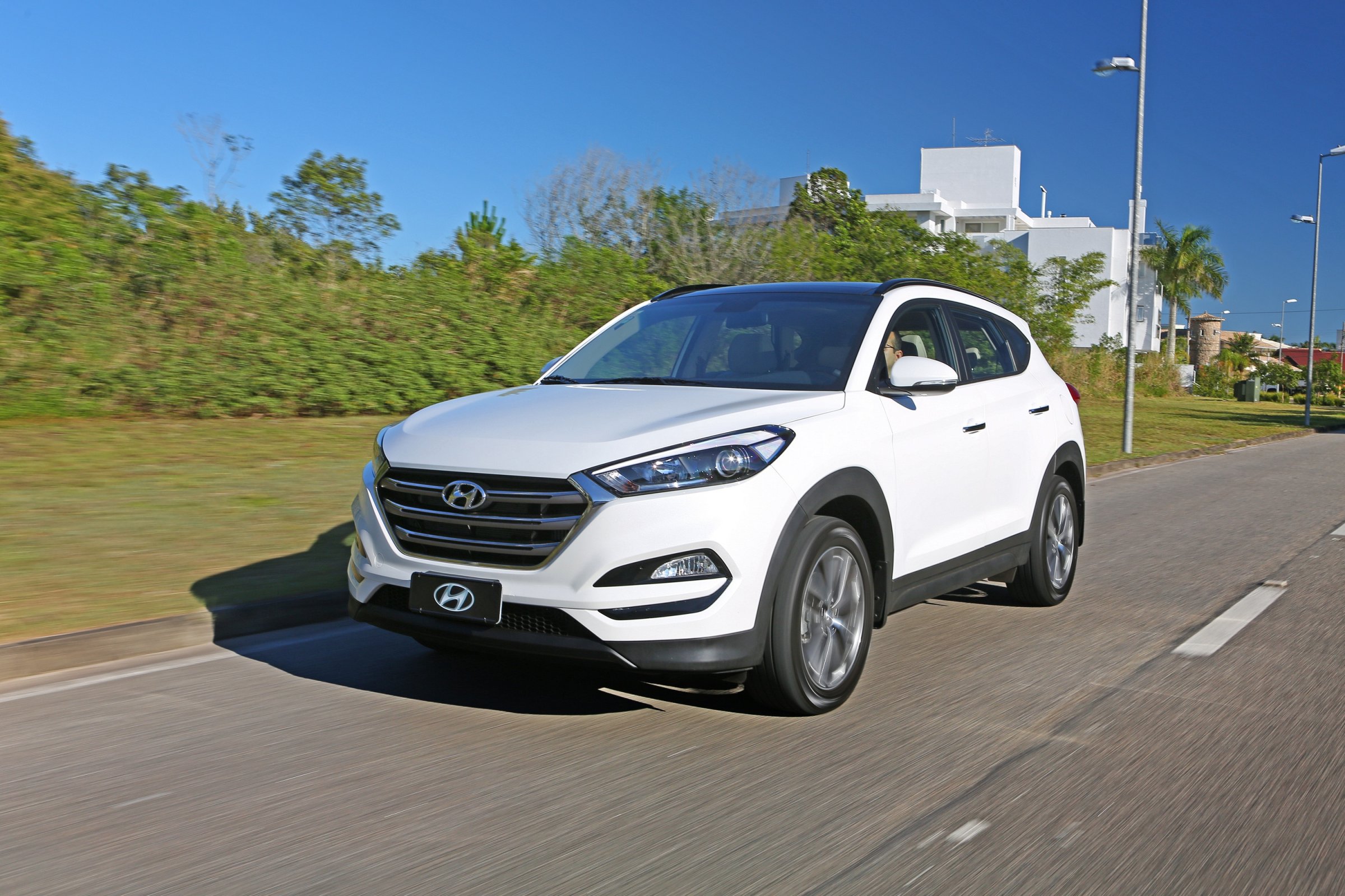 Hyundai Tucson branca estacionada em estrada asfaltada com céu azul e algumas árvores ao fundo