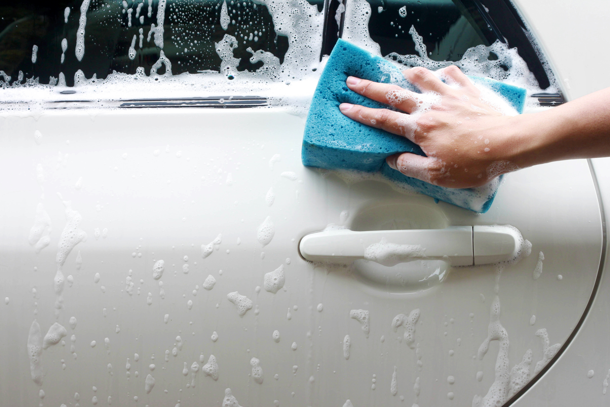 Pessoa passa esponja sobre lataria do carro para lavar o veículo com água e sabão