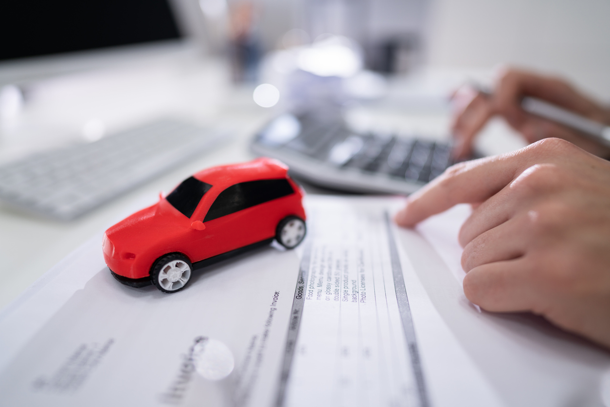 Homem fazendo contas em calculadora com carro vermelho de brinquedo em cima da mesa