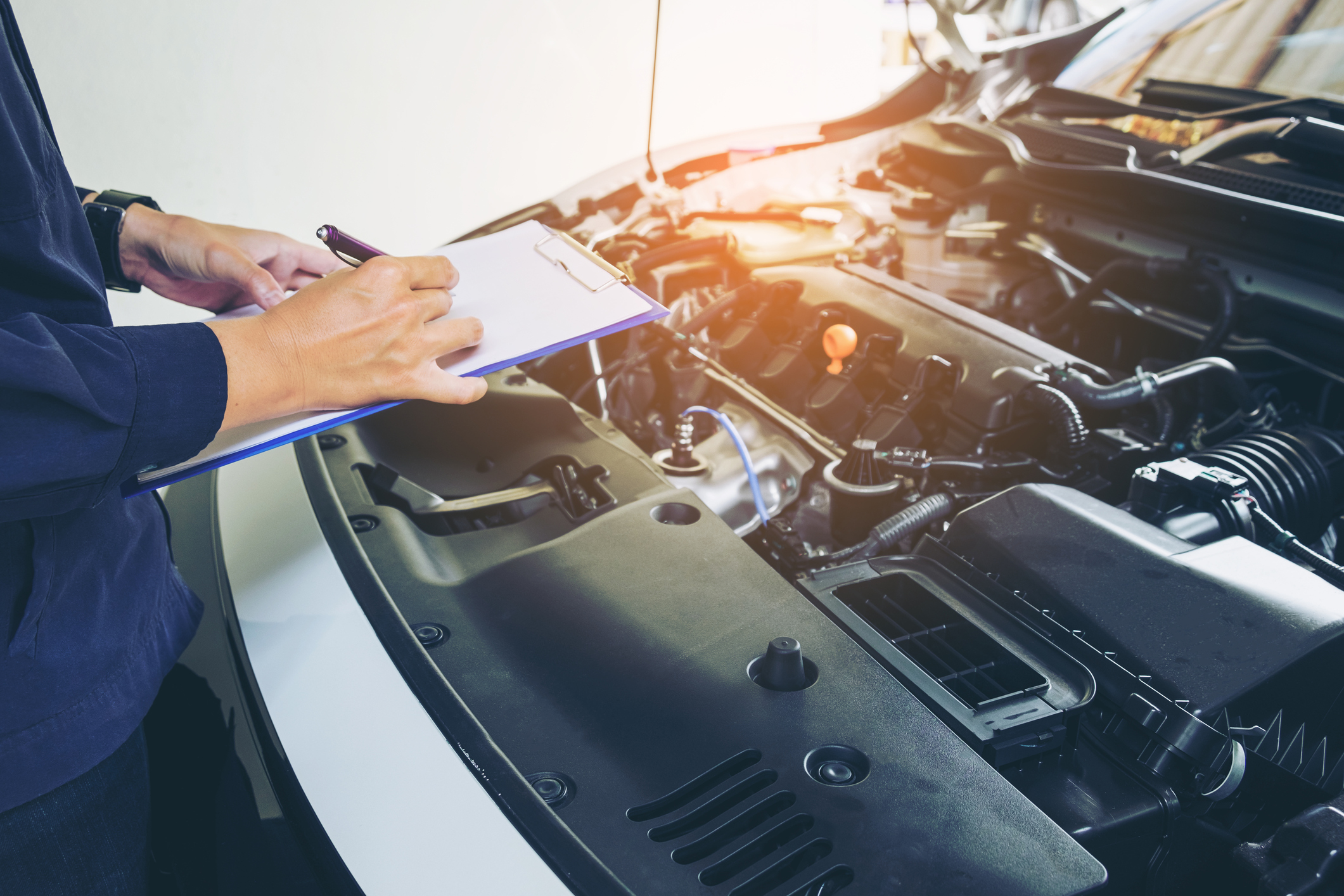 Imagem mostra um homem fazendo anotações na prancheta durante a revisão de um carro