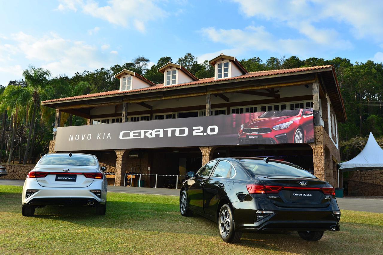 Dois Kia Cerato de traseira, um branco e outro preto, lado a lado em frente a uma construção