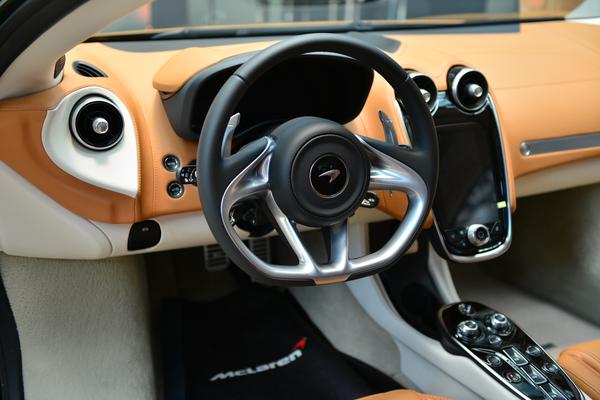 Cabine do McLaren GT tem painel na cor da caroceria laranja, volante com base chata e acabamento em aço escovado e uma tela multimídia vertical ao centro