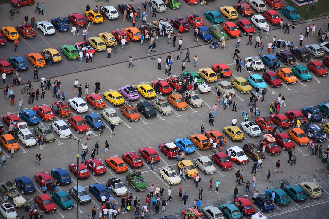 Foto aérea mostra pátio repleto de carros lado a lado e dezenas de pessoas olhando