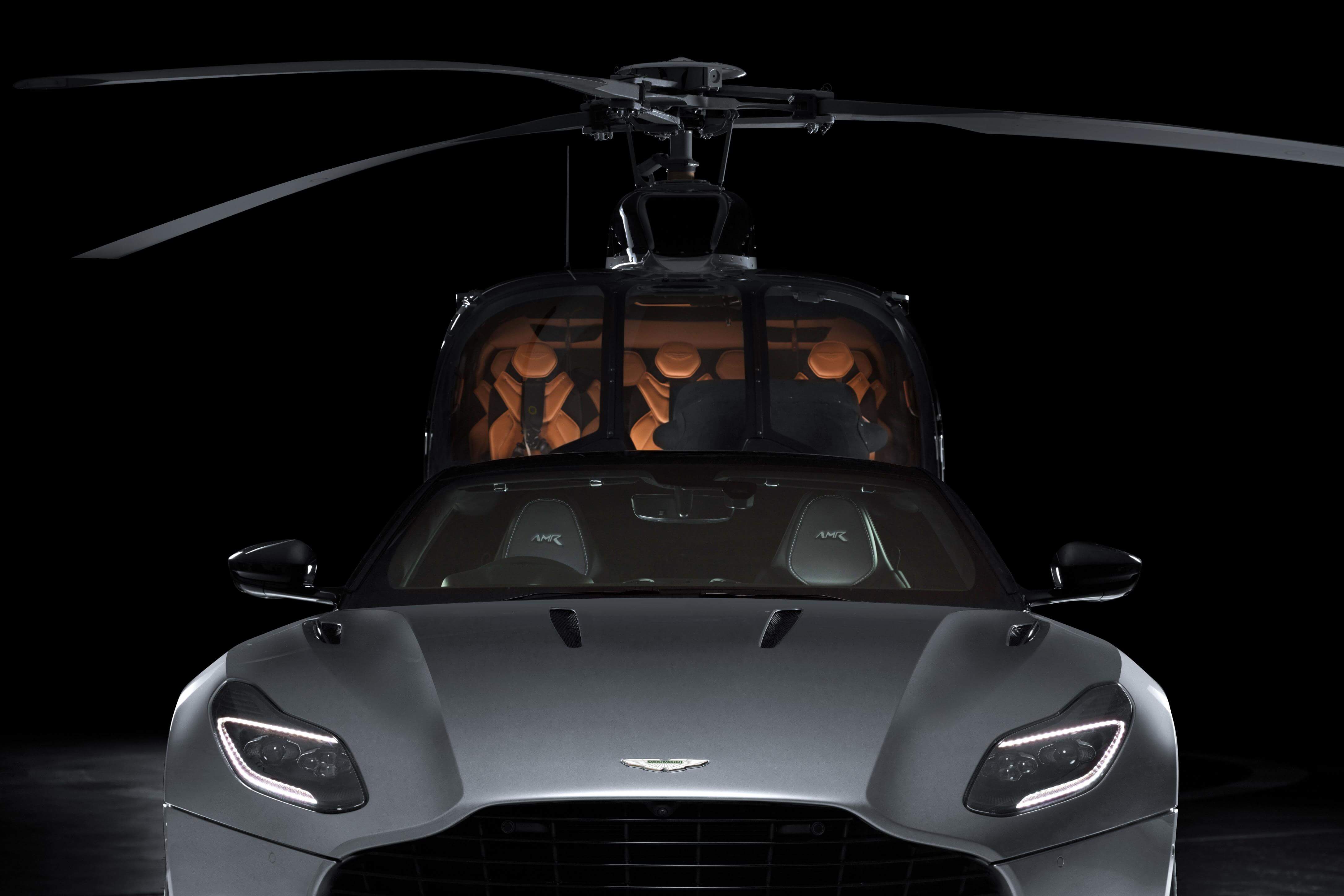 O carro Aston Martin DB11 prata e o helicóptero ao fundo