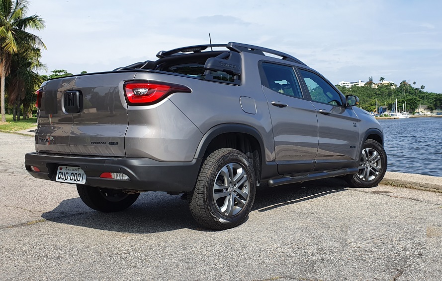 Fiat Toro na cor cinza escuro de traseira com marina de barcos ao fundo