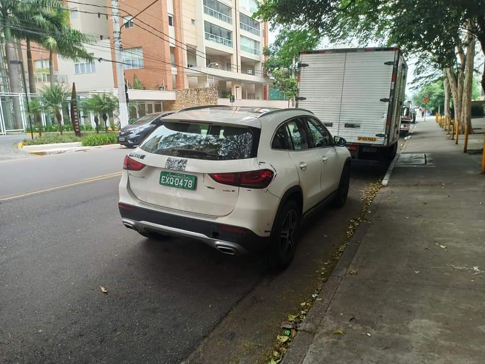nova mercedes gla com placa verde de traseira na cor branca e com adesivo cobrindo a marca da estrela estacionado em uma rua