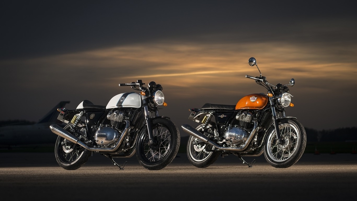 Royal Enfield Continental GT com tanque branco à esquerda e Interceptor com tanque amarelo à direita, lado a lado com o entardecer ao fundo