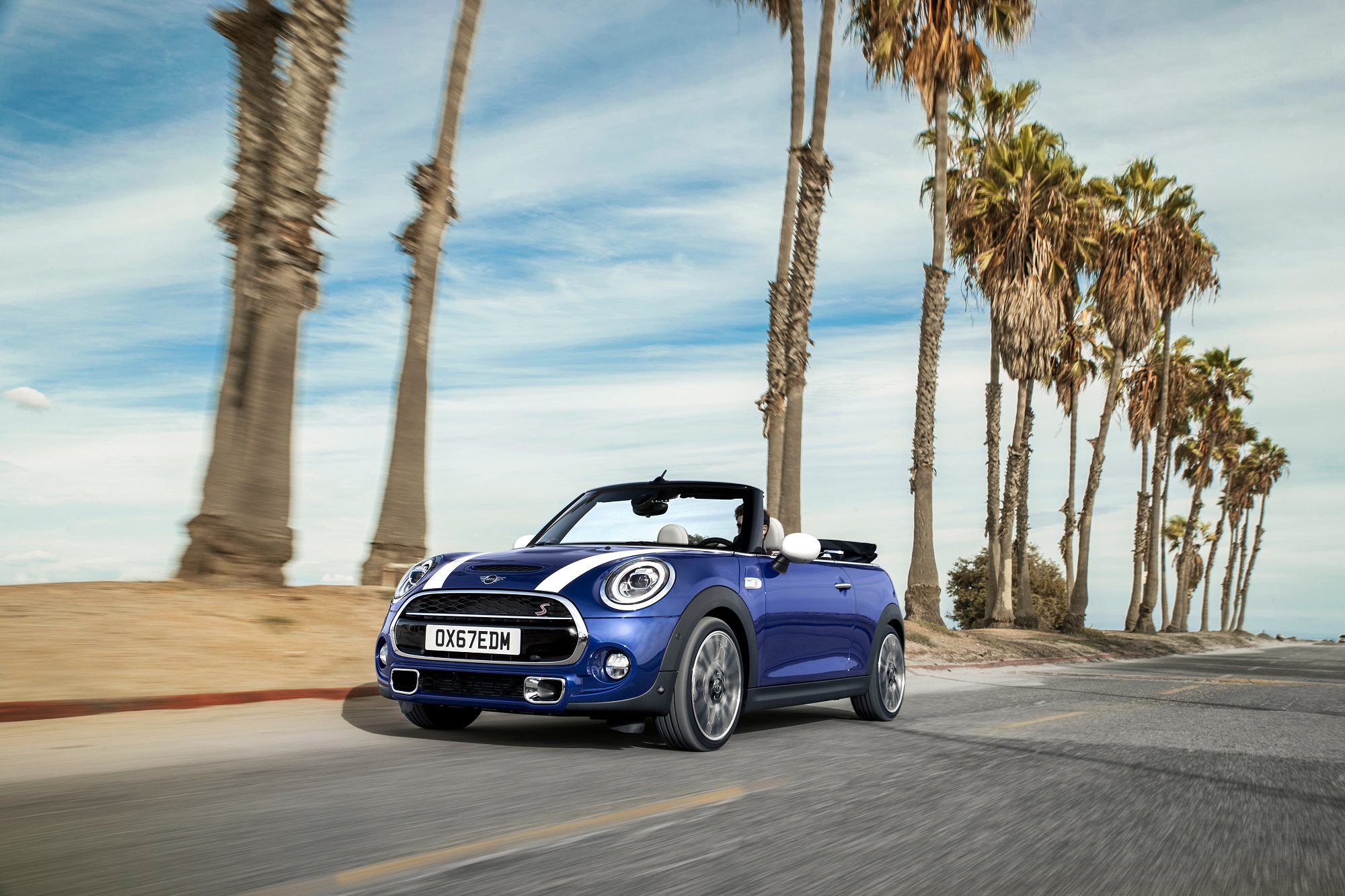 Mini Cooper Cabrio S em movimento de frente com capota aberta e estrada margeada de palmeiras no litoral