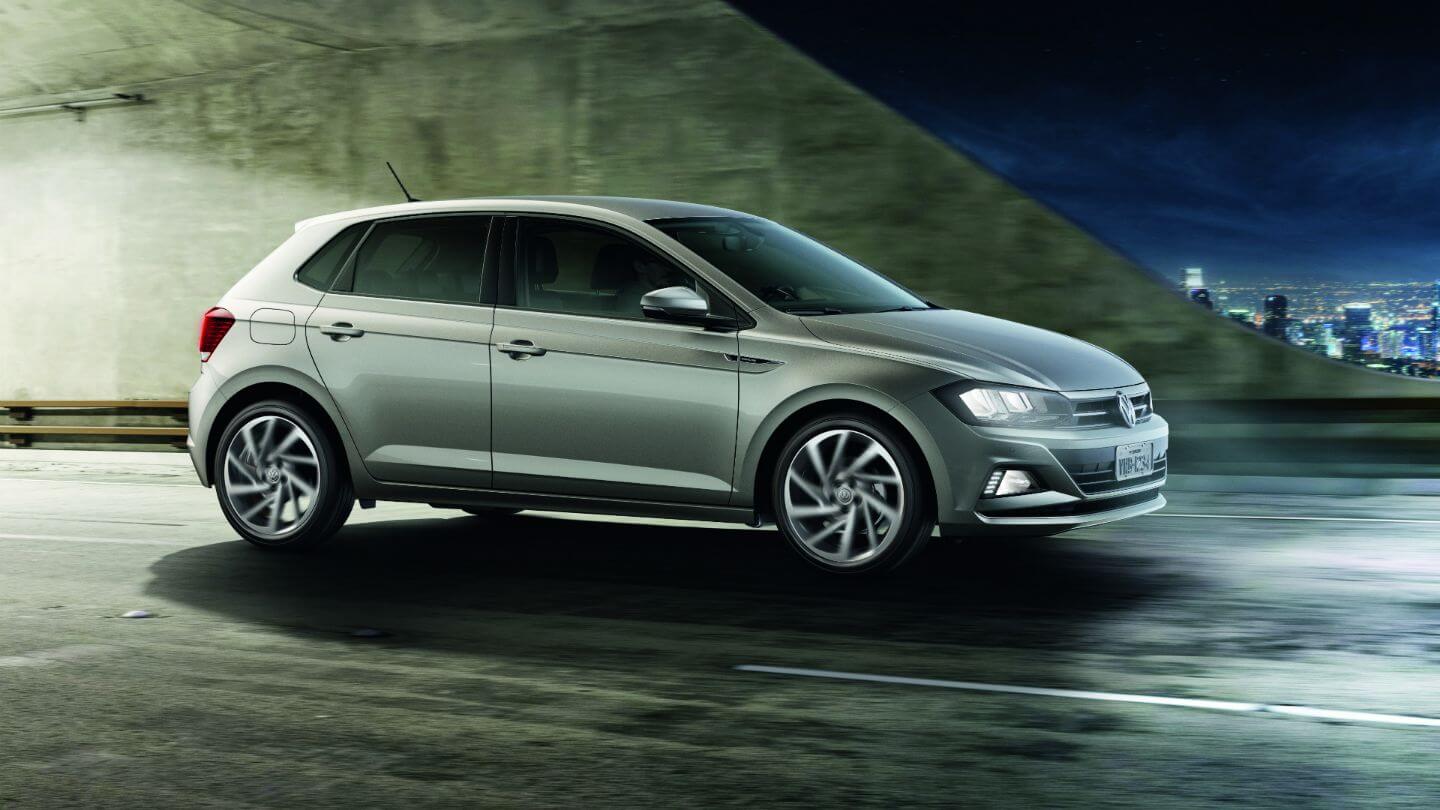 Vw Polo na cor prata metálico de perfil com os faróis acesos