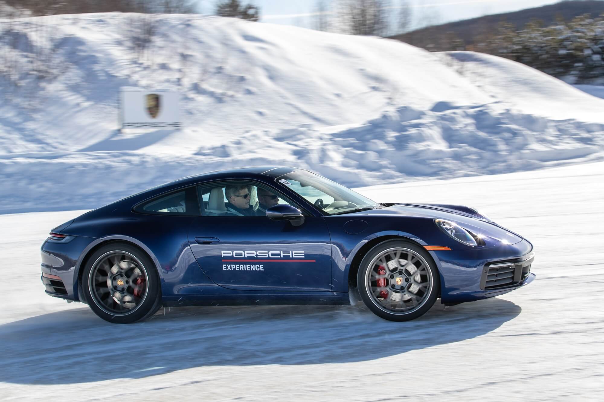 Porsche 911 azul andando meio de lado na neve