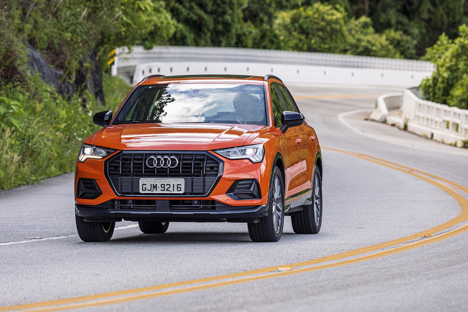 Audi Q3 laranja em movimento na curva e ao fundo a estrada sinuosa