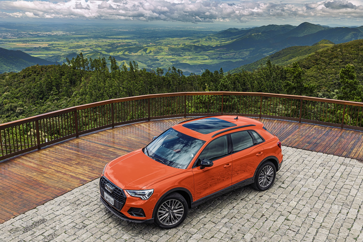Audi Q3 laranja parado visto de cima com teto-solar e ao fundo um vale cercado de verde