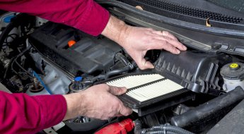 Homem checa o filtro de ar dentro do compartimento do motor do carro
