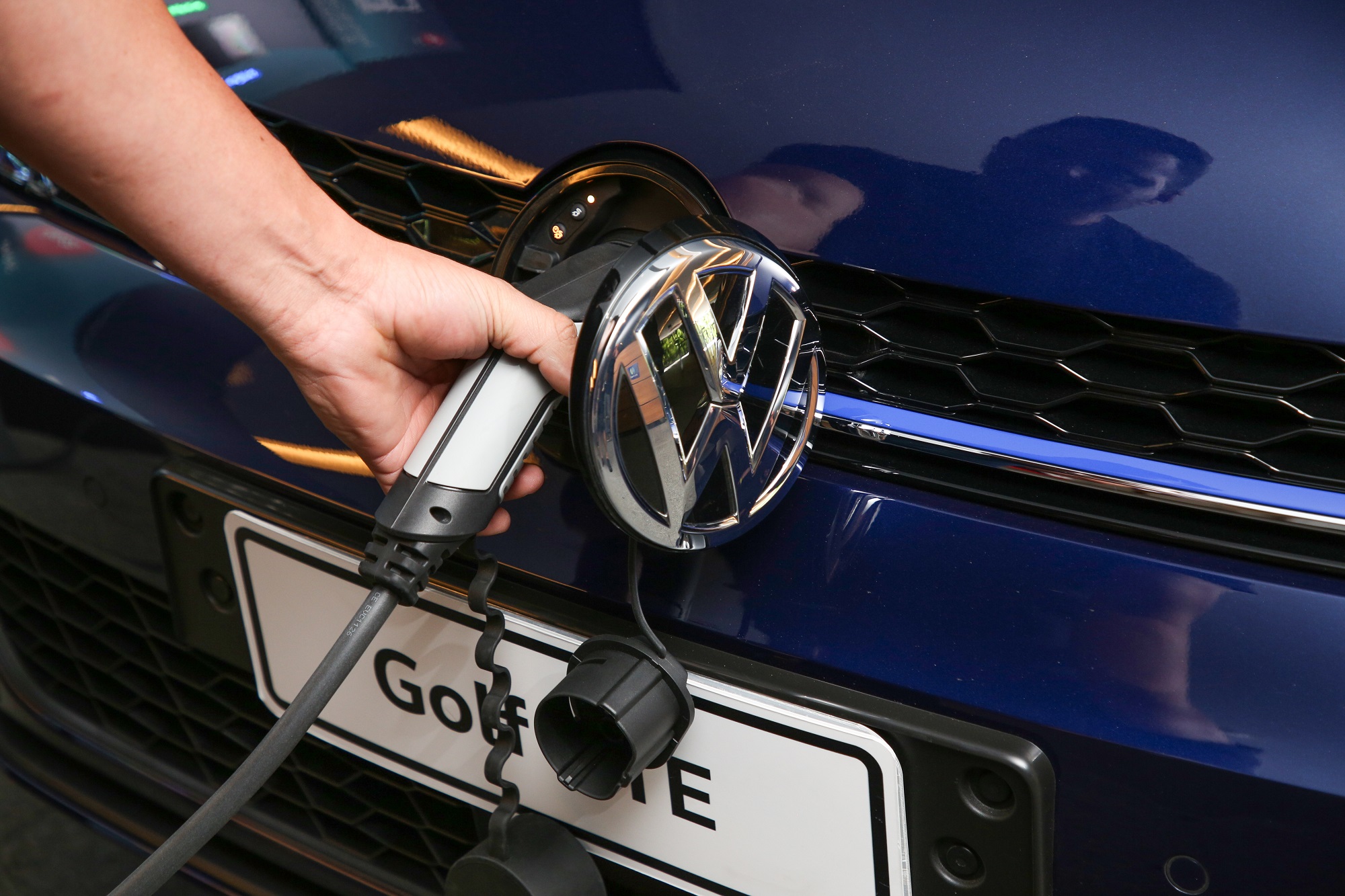 Volkswagen Golf Gte sendo carregado com plugue instalado na grade dianteira, cujo logo da marca serve como porta para a tomada