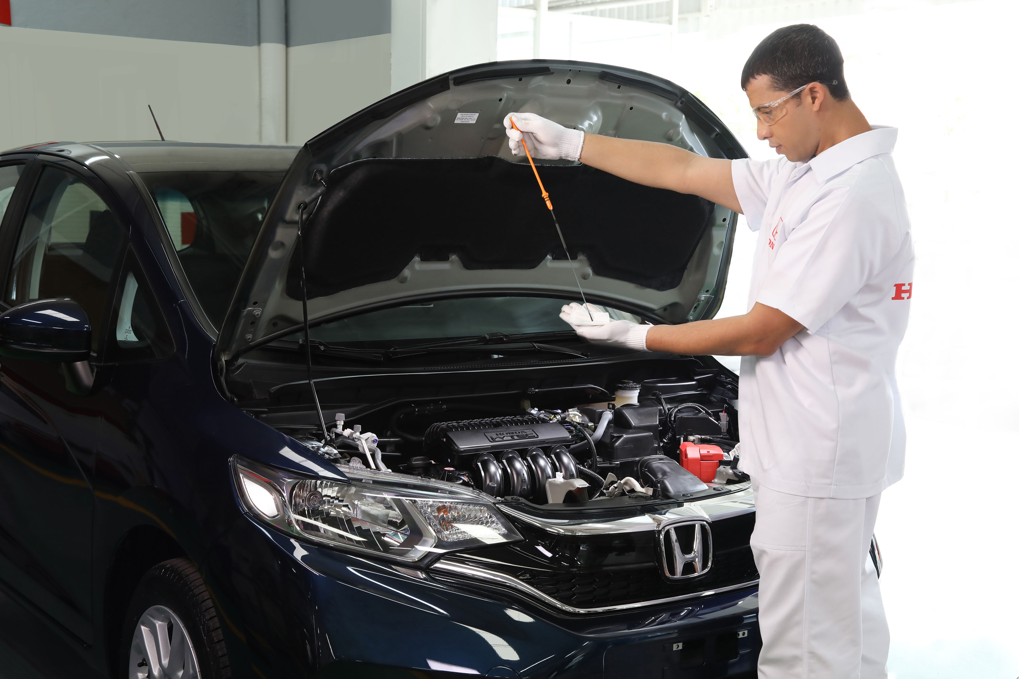 Profissional da Honda verifica o óleo de um carro com capô aberto