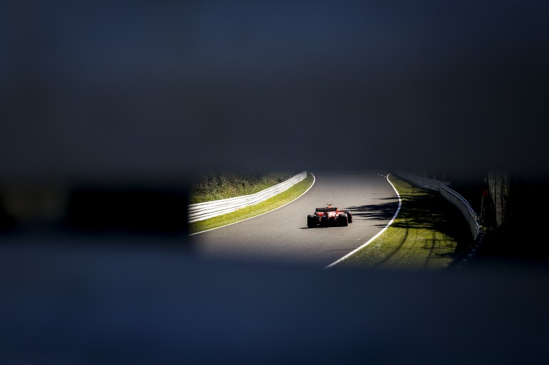 Foto de um carro de fórmula um no GP do Japão tirada da abertura de um guard rail