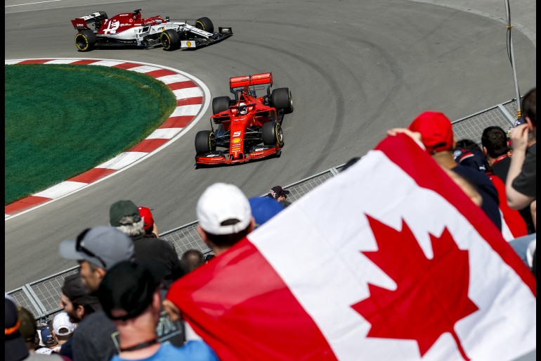 Homem com bandeira do Canadá observa dois carros de fórmula 1 fazendo a curva durante o GP do Canadá, em Montreal