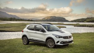 Fiat Argo Trekking branco com faixa preta sobre o capô estacionado em frente a um lago e ao fundo uma montanha