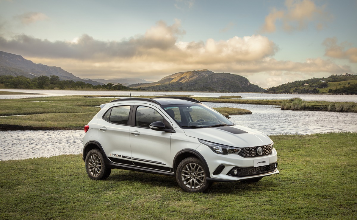 Fiat Argo Trekking branco com faixa preta sobre o capô estacionado em frente a um lago e ao fundo uma montanha