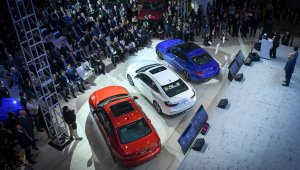 Imagem de cima mostra coletiva de imprensa do Salão De Detroit 2019 com apresentador em um palco ao lado de três caros e vários jornalistas acompanhando