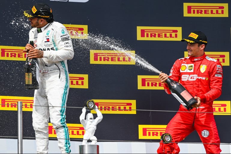 Charles Leclerc, de macacão vermelho da Ferrari no terceiro lugar do pódio do Gp Da França 2019 espirra champanhe em Lewis Hamilton, de macacão branco da Mercedes, no lugar mais alto do pódio