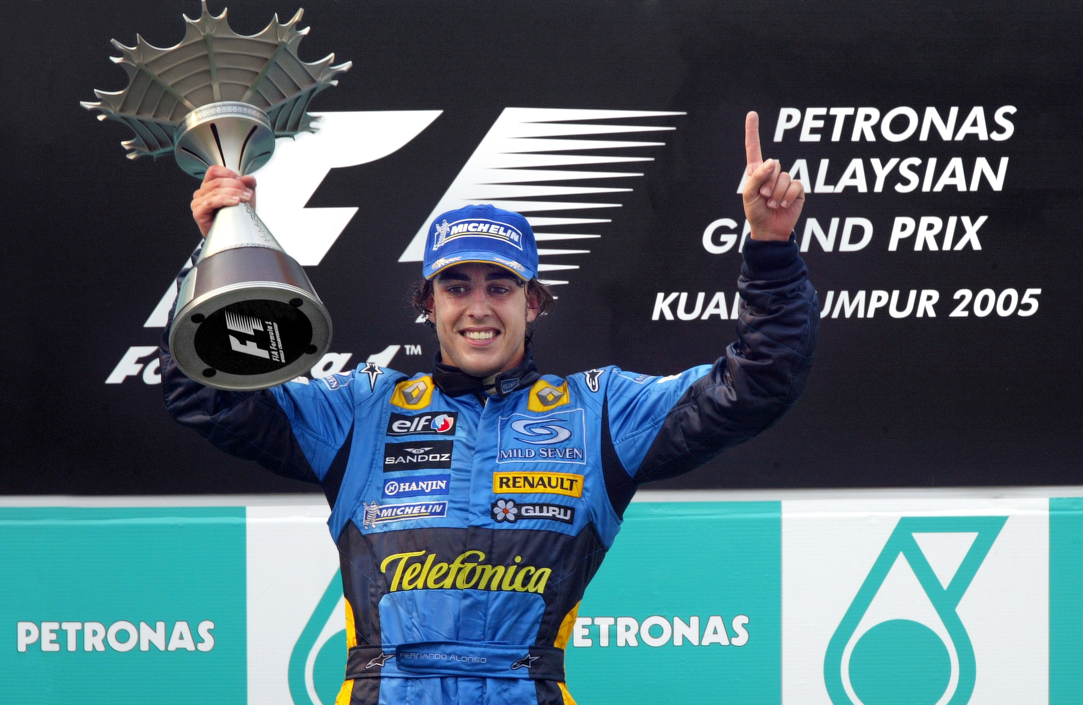 Com macacão azul da Renault, Fernando Alonso segura o troféu de vencedor em cima do pódio no Grande Prêmio da Malásia