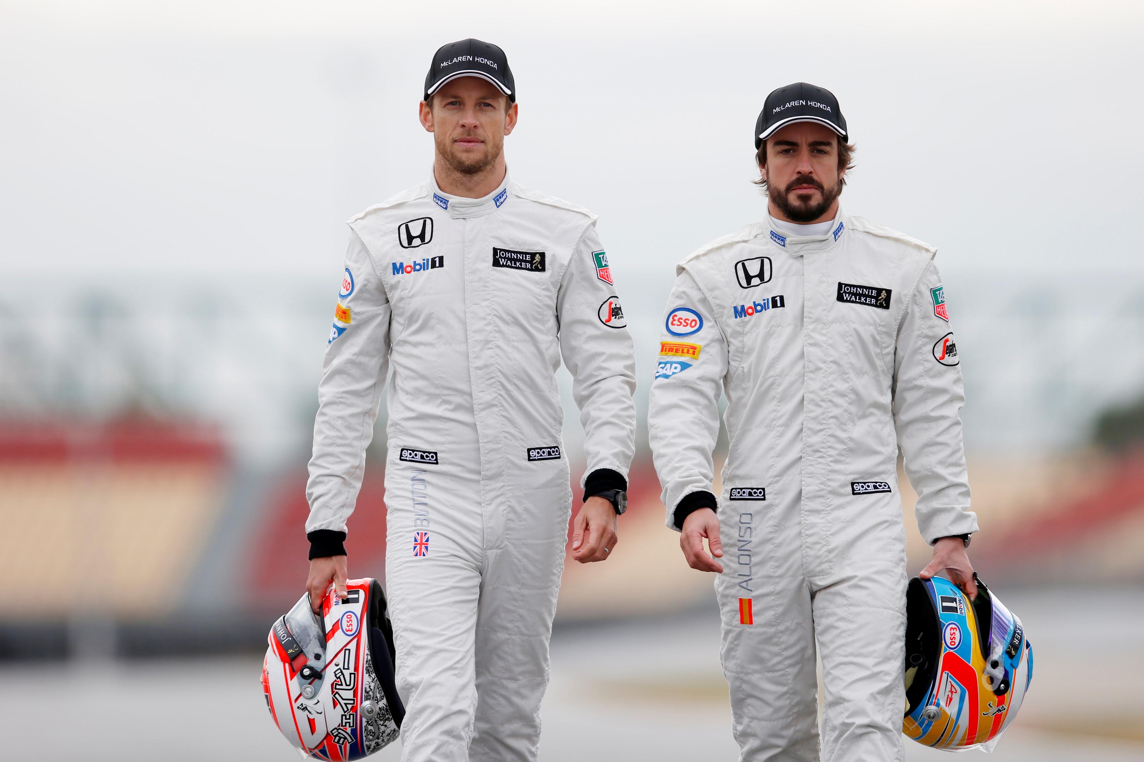 Jason Button e Fernando Alonso Na Mclaren com macacões brancos da escuderia e capacetes na mão, caminham em um circuito lado a lado