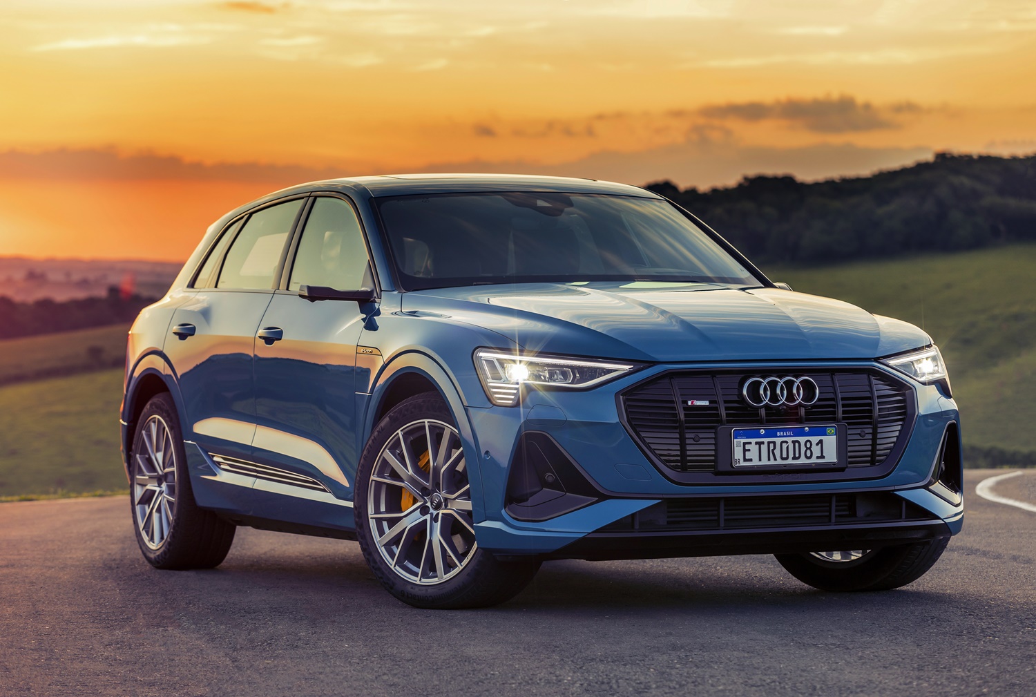 Audi E Tron azul de frente com faróis acesos ao fundo entardecer atrás das montanhas