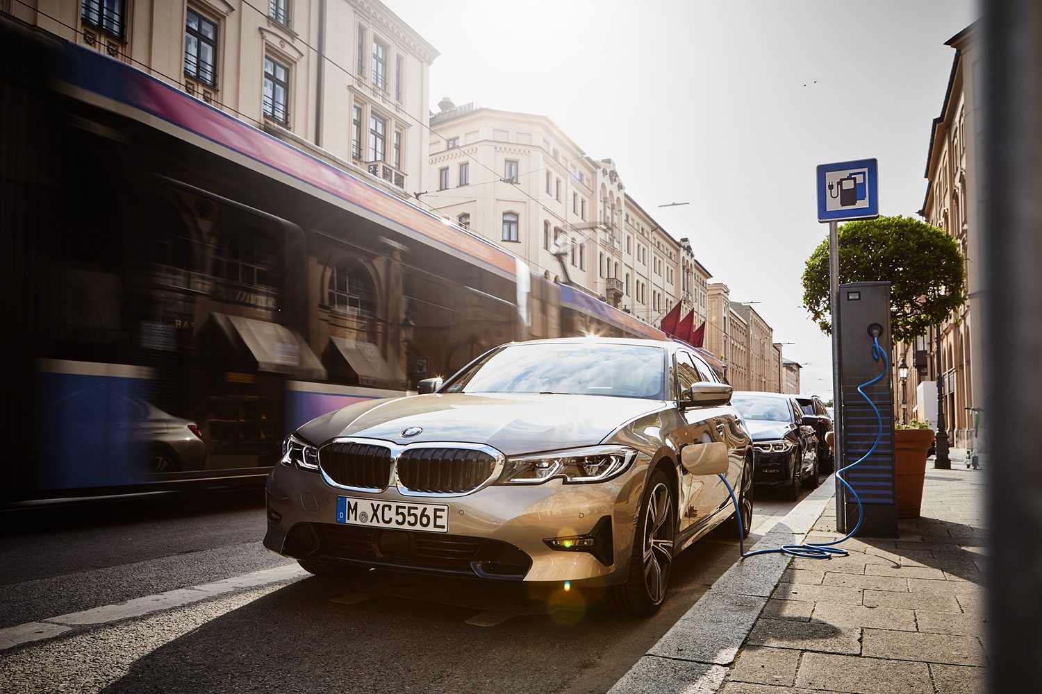 Bmw Série 3 Híbrido dourado estacionado em uma rua sendo carregado em um ponto de recarga