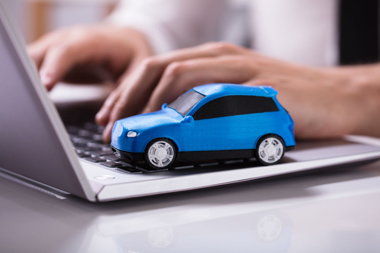 Carro em miniatura azul no teclado de Laptop e mulher digitando aparelho