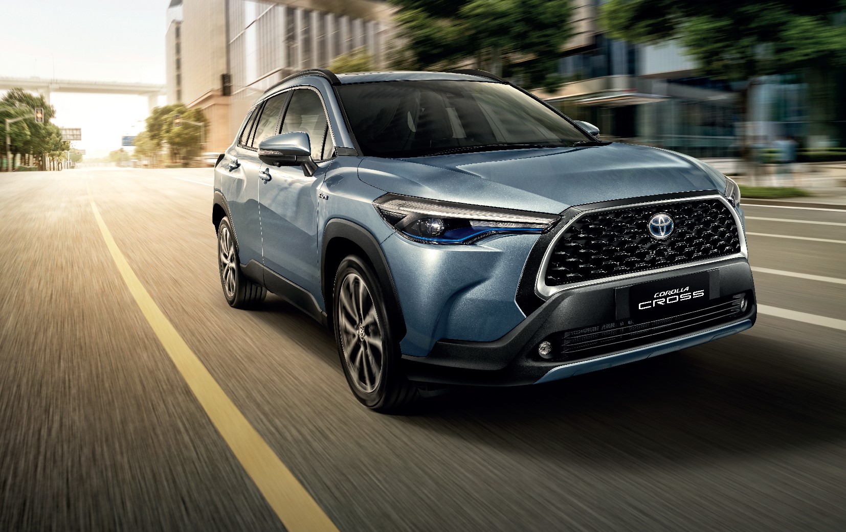 Toyota Corolla Cross na cor azul de frente em movimento numa rua repleta de prédios com o fundo distorcido