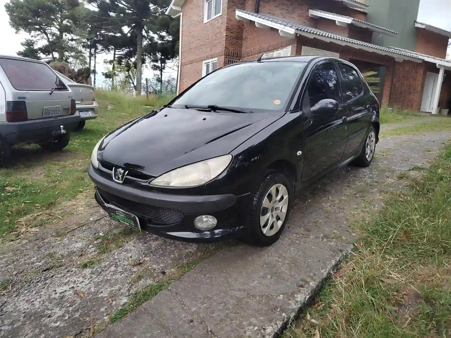 Carro Peugeot 206 usado à venda por até 15 mil reais, preto, em boas condições, estacionado em área residencial com outros veículos ao fundo.