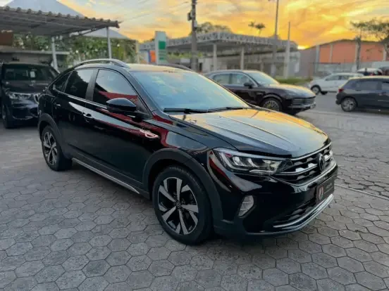 Volkswagen Nivus preto estacionado em concessionária ao pôr do sol, com fundo de carros e céu colorido.