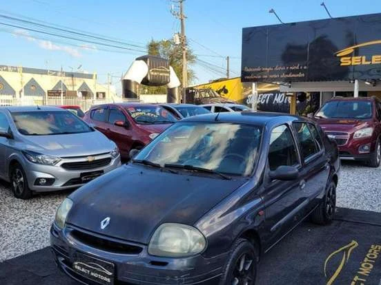 Renault Clio usado à venda por até 12 mil reais, estacionado em concessionária com outros veículos ao fundo.