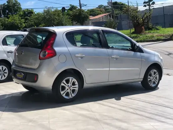FIAT Palio usado por até 30 mil reais, em excelente estado, estacionado ao ar livre em um terreno de estacionamento, com fundo de árvores e céu claro.