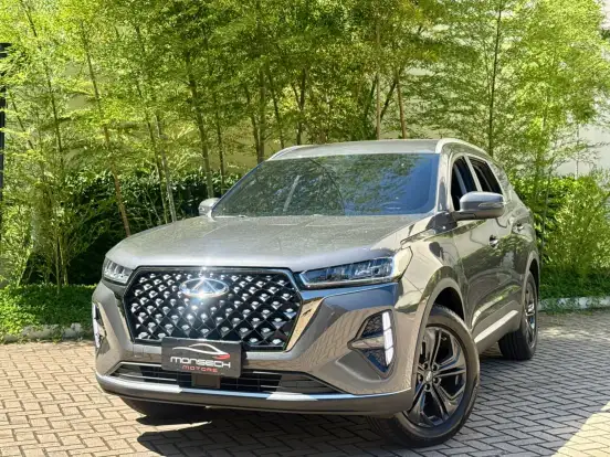 Caoa Chery Tiggo 7 em uma estrada rodeada de árvores verdes, destaque para seu design moderno e linha elegante, ótimo custo-benefício até 150 mil.