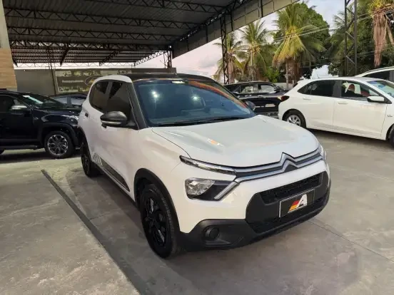 Citroën C3 branco em uma concessionária, destaque para seu design moderno e compacto, com preço acessível até 70 mil. Ótima oportunidade de compra.