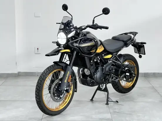 Imagem da motocicleta Royal Enfield Himalayan 450 Hangl Black exibida em ambiente interno, destaque para o design robusto, rodas douradas e proteção contra água.