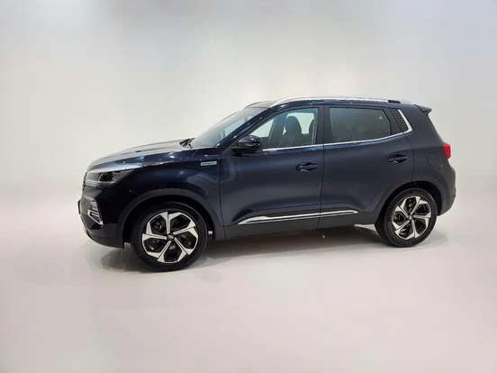 Imagem do SUV CAOA Chery Tiggo 5X Pro na cor azul escuro, exibido em uma sala com fundo neutro, destacando seu design moderno, detalhes em cromado e rodas de aros esportivos.