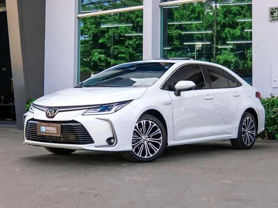 Toyota Corolla branco em destaque na frente de uma loja de carros, ideal para quem busca um carro econômico até 150 mil reais.