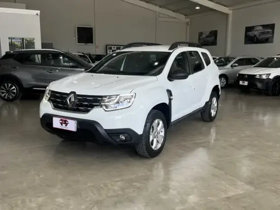 Imagem de um Renault Duster branco, carro SUV compacto ideal até 100 mil, exibido em showroom com outros veículos ao fundo, destaque para o modelo acessível.
