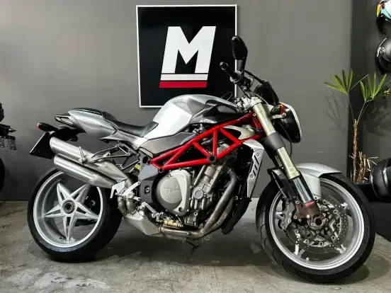 Imagem de uma motocicleta MV Agusta Brutale 910S em cinza, com estrutura vermelha, em showroom, destacando seu design esportivo e potente motor.