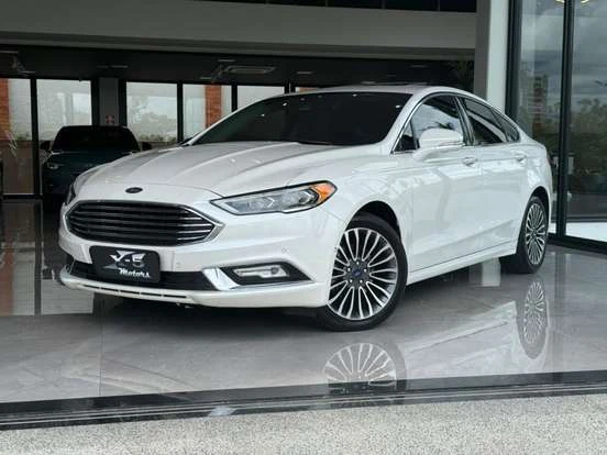 Ford Fusion branco em excelente estado dentro de uma concessionária, com preço até 100 mil reais. Carro sedã robusto, confortável e com bom custo-benefício.