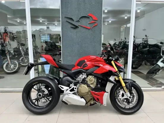 Imagem de uma Ducati Streetfighter V4 S vermelha e preta exibida em uma concessionária, com design esportivo, detalhes aerodinâmicos e preço até 100 mil reais.