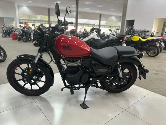 Imagem de uma moto Royal Enfield Meteor 350 na cor vermelha, exibida em uma concessionária com outros modelos de motos ao fundo, perfeita para quem busca uma motocicleta nova até 50 mil reais.